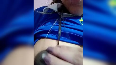 Media: A video of a close-up of a woman's arm, with a tattoo needle being inserted into her upper arm, partially covered by a blue t-shirt. The background is out of focus, featuring blurred blue fabric.