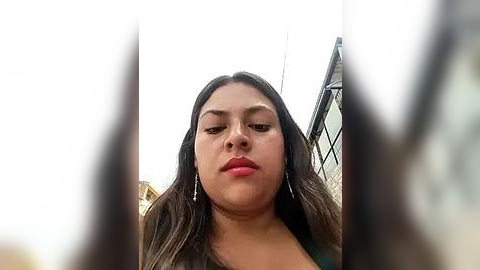 Media: Video of a Latina woman with medium skin tone and long, wavy dark hair, wearing a black top, standing in an urban setting.