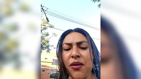 Media: Video of a woman with wet, shoulder-length brown hair and light skin, looking serious outdoors. Power lines and trees in background.