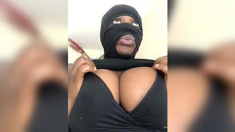 Media: A video of a Black woman with dark skin, large breasts, wearing a black mask, and a black dress, holding up the dress to expose her cleavage, taken from a low angle.