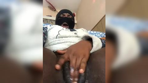 Media: Video of a dark-skinned person in a white hoodie, black mask, and gloves, masturbating, in a dimly lit room with blurred background.