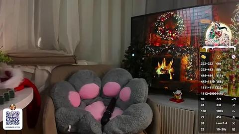 Media: Video of a cozy living room with a plush gray teddy bear in a Santa hat, a lit fireplace, Christmas decorations, and a television screen showing a camera view.