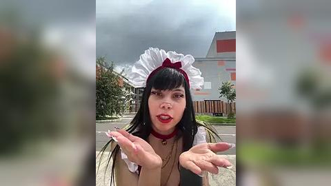 Media: A video of a woman in a maid costume with a frilly white headpiece and red accessories, outdoors on a cloudy day.