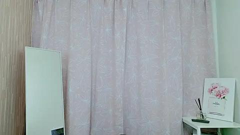 Media: A video of a minimalist room with light pink floral-patterned curtains, a white mirror, and a small white desk with a floral print on it and a pen holder.