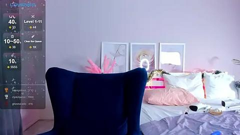 Media: A video of a bedroom with a dark blue velvet chair, a pink flower arrangement, white bed with pink pillows, and framed art on a light pink wall.