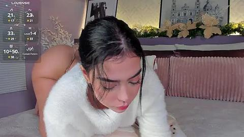 Media: Video of a woman with dark hair and fair skin, wearing a white sweater, on all fours on a bed, in a room with a radiator and potted plants.