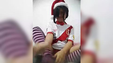 Media: A blurry video shows a person wearing a red Santa hat and white shirt with a red sash, seated between two people with striped stockings.