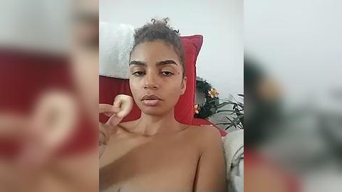 Media: A video of a young Black woman with curly hair, partially topless, lying on a red cushion, applying makeup with a red lipstick.