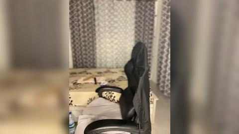 Media: Video of a messy bedroom with a black jacket draped over a bed, patterned wallpaper, and scattered clothes on the floor.