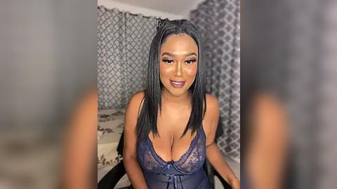 Media: Video of a curvy, light-skinned Black woman with long black hair, wearing a sheer purple lace lingerie bodysuit, sitting in a dimly lit room with patterned wallpaper.