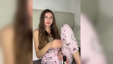 Media: A video of a young woman with long brown hair in pink pajamas sitting on a bed, blurred background.