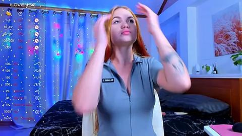 Media: Video of a blonde, fair-skinned woman in a blue button-up shirt, adjusting her hair in a modern bedroom with colorful curtains, a bed, and a potted plant.