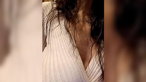 Media: Video of a woman's chest with wet, dark hair and a white ribbed sweater, blurred background.