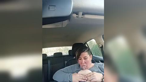 Media: A video captures a woman, possibly in her 30s, with short brown hair, wearing a gray shirt, breastfeeding in the backseat of a car, with blurred background.