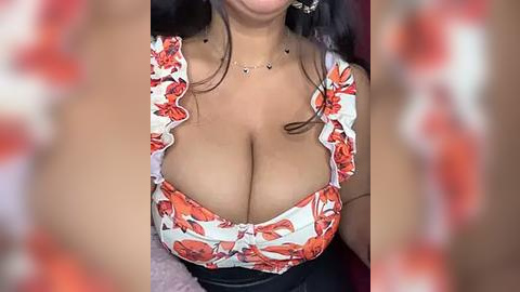 Media: Video of a woman with medium brown skin, wearing a low-cut, floral-patterned top revealing ample cleavage, and a black skirt. Her long, dark hair cascades down her shoulders.