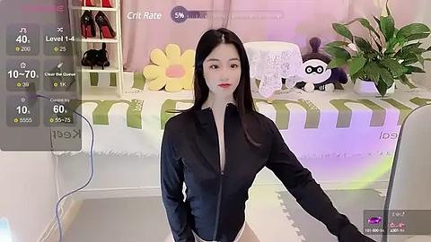 Media: A video captures a young Asian woman with long black hair, wearing a black button-down shirt, standing in a colorful bedroom with a white bed, green striped blanket, and panda plush toys.