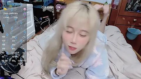 Media: A blurry video of a young woman with blonde hair and a light-colored hoodie, lying on a bed in a messy room with wooden furniture.