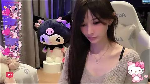 Media: Video of a young woman with long dark hair, wearing a beige sweater, sitting on a white gaming chair. Background includes plush toys, dim lighting, and a \"Hello Kitty\" filter overlay.