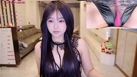 Media: A video of an Asian woman with long black hair, wearing a black lace top, standing in a modern living room. A close-up inset shows her genital area with a pink vibrator inserted.