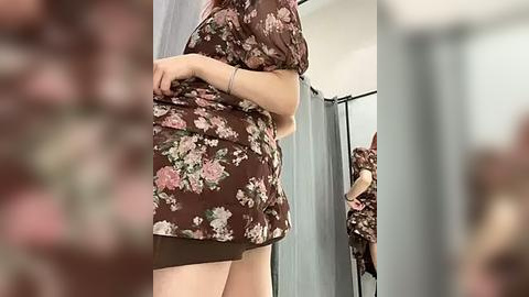 Media: Video of a woman in a floral dress, lifting the hem, revealing a glimpse of her thighs. She stands in a mirror-lit dressing room with a blurred background.