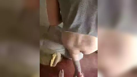 Media: A blurry video showing a person wearing grey pants and socks, bending over, with a banana on the floor.