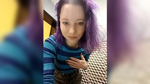 Media: Video of a young woman with purple hair, wearing a blue and black striped top, standing in a room with a yellow wall and black-and-white patterned rug.