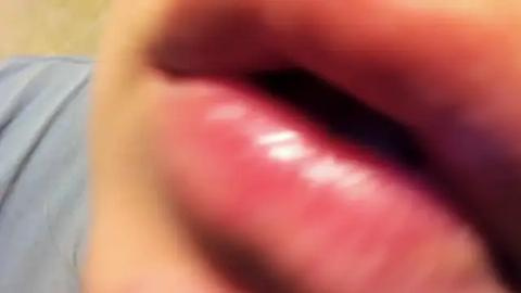 Media: Video of a close-up of a person's open mouth, showing pinkish-red, shiny, moist tongue with visible saliva, partially obscured by blurry lips and blurred background.