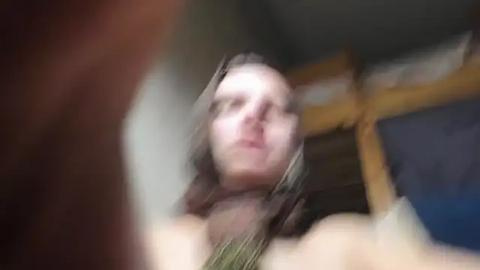 Media: Blurry video of a person with shoulder-length hair, wearing headphones, facing downward, in a dimly lit room with a wooden bed and blue wall.