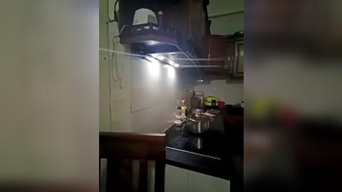Media: Video of a dimly lit kitchen with a hanging black pot above a cluttered counter. The counter holds various items, including a jar of peanut butter, and a green object is partially visible in the background.