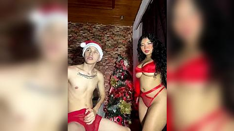 Media: Video of a shirtless, tattooed man in red underwear and a Santa hat, standing beside a curvy woman in red lingerie, in a festive room with a decorated Christmas tree.