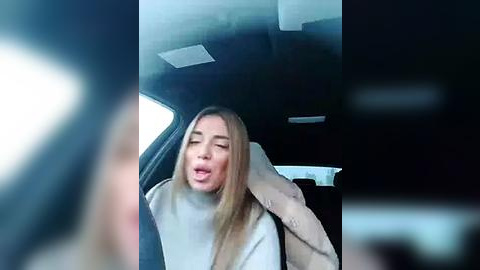 Media: A video captures a young woman with long, straight blonde hair, eyes closed, mouth open, wearing a white turtleneck, seated in a car with blurred surroundings.