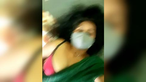 Media: Video of a woman with long black hair, wearing a green saree, pink top, and face mask, blurred background, motion blur effect, candid shot.