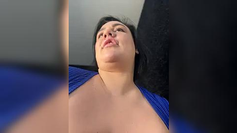 Media: A video of a woman with dark hair, wearing a blue top, lying on her back, with a blurred background featuring a black and blue patterned surface.