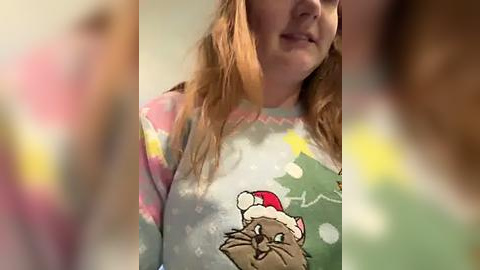 Media: A blurry video of a woman with long, wavy hair wearing a festive, cartoon-themed Christmas sweater featuring a bear. The sweater has a mix of pastel colors and playful patterns. The background is out of focus.