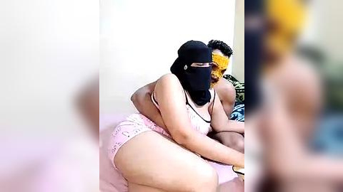 Media: Video of a plus-sized woman in pink lace panties, embracing a muscular man with a black mask, in a bedroom with a yellow wall and pink bedspread.