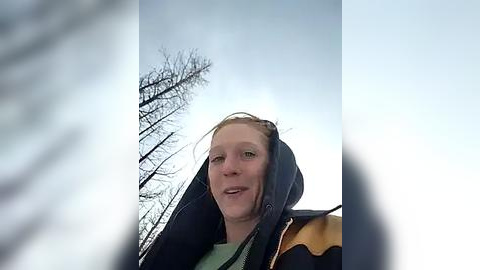 Media: Video of a smiling Caucasian woman with light brown hair in a dark winter coat, standing in a snowy, treeless landscape with a bright sky.