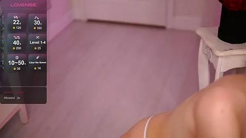 Media: Video of a woman lying on a bed, with a smartphone displaying \"LOVENSE\" in the corner. The room has soft pink walls and a white nightstand.