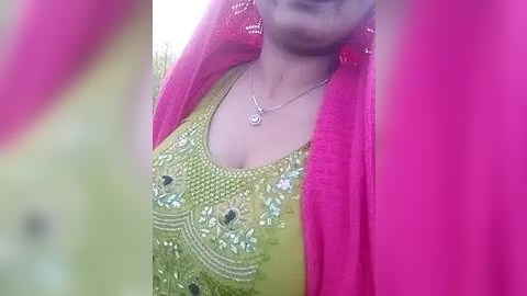 Media: Video of a woman in a bright yellow embroidered top and pink dupatta, with a silver necklace, smiling slightly.