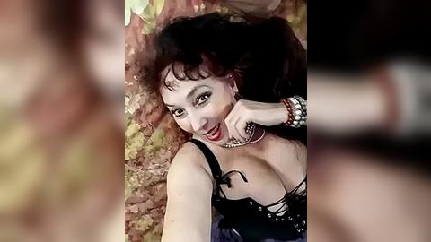 Media: A video of a woman with long, dark hair, wearing a black corset and a choker, lying on a bed of autumn leaves.