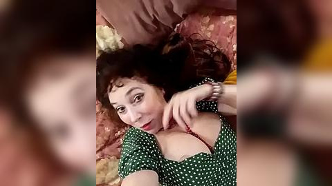 Media: A blurry video shows a woman with curly hair and red lipstick, lying on a bed, unbuttoning her green polka-dotted blouse, revealing cleavage.