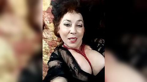 Media: Video of a voluptuous, fair-skinned woman with red lipstick, wearing a black lace robe with a red polka dot bralette, reclining against a floral-patterned backdrop.