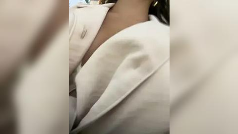 Media: Video of a close-up of a person's neck and shoulders, wearing a white bathrobe, with a blurred background. The texture of the robe is soft and plush.