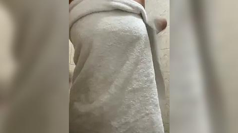 Media: A video of a person wrapped in a white towel, standing in a beige-tiled bathroom. The towel covers their lower body, with blurred out faces on either side.