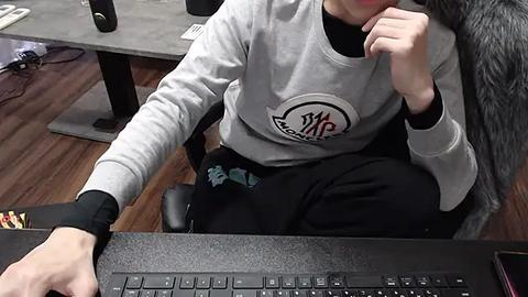 Media: A video shows a person in a gray sweatshirt typing on a black keyboard. They have a gray cat on their lap. The background features a wooden floor and a desk with a mouse and keyboard.