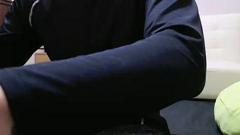 Media: A close-up video of a person in a dark navy blue long-sleeved shirt, seated, with a light green pillow and a white surface visible in the background.