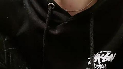 Media: Video of a person wearing a black hoodie with a graphic design, showcasing a close-up of their neck and chest. The hoodie's fabric appears soft and cozy.