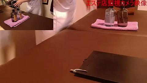 Media: Video of a spa treatment room with a massage table covered in brown leather, two glass bottles, and a cloth, and a person in a white robe preparing oil.