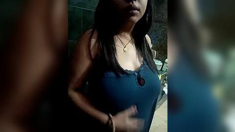 Media: Video of a woman with long black hair, wearing a blue lace-trimmed tank top, standing outdoors against a dimly lit background.