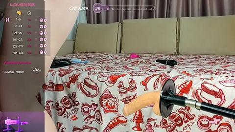 Media: Video of a virtual reality scene featuring a man's erect penis being inserted into a realistic-looking sex toy. Background shows a beige bed with red patterned sheets.