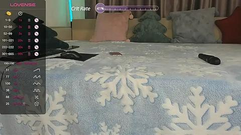 Media: Video of a bed with a white snowflake-patterned blanket, three pillows in pink, gray, and teal, and a black vibrator on the left side, taken from a first-person perspective.